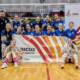 Zdjęcie drużyny siatkarek pozującej w hali sportowej po meczu – zawodniczki w niebieskich strojach wraz z trenerem trzymają baner „Kibicuj z Miastem Żory”, prezentując radość i sportowe emocje po wspólnej rywalizacji.