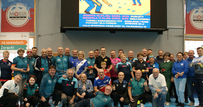 Galeria zdjęć z turnieju sportowego seniorów w hali MOSiR przedstawia uczestników w sportowych koszulkach podczas wręczania pucharów i dyplomów, wspólne fotografie zwycięzców oraz momenty dekoracji na tle siatki i hali sportowej.