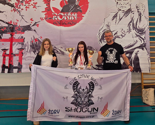 Galeria przedstawia zawodników klubu Shogun podczas turnieju karate kyokushin. Na zdjęciach widoczne są walki na macie, prezentacje kata, dekoracje medalowe oraz wspólne fotografie uczestników i trenerów.