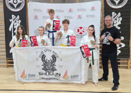Galeria zdjęć z wydarzenia sportowego odbywającego się w hali. Widoczni są uczestnicy w strojach do sztuk walki, pokazy, wspólne ustawienia zawodników oraz wręczanie nagród.
