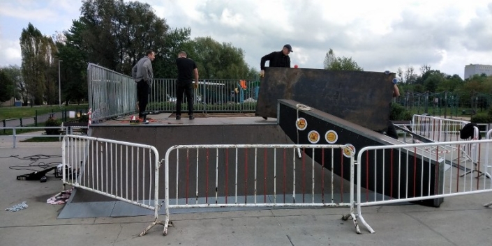 Zdjęcie przedstawia uszkodzony obiekt na miejskim Skateparku i ekipę naprawiającą obiekt