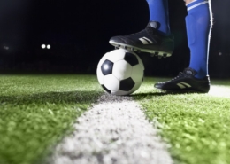 Na zdjęciu nogi piłkarza przytrzymujące piłkę nożną na murawie boiska
