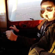 Na zdjęciu Franek Krakowczyk siedzący za sterami samolotu, w okularach przeciwsłonecznych i słuchawkach