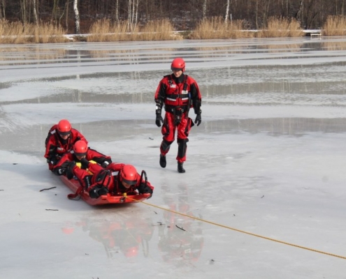 Na zdjęciu grupa strażaków ćwiczy wyciąganie z wody topielca na zamarzniętym Śmieszku