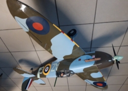 Na zdjęciu model samolotu Spitfire w kolorze moro khaki-niebieski stojący na podłodze