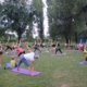 Na zdjęciu zajęcia z jogi na trawie, ćwiczący na matach