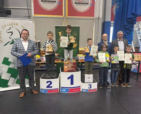 galeria zdjęć przedstawia zwycięzców zawodów szachowych na podium w żorskiej hali sportowej