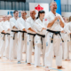 Zdjęcia przedstawiają treningi i pokazy karate, zarówno w hali sportowej, jak i na świeżym powietrzu, z udziałem wielu osób w białych strojach, wykonujących ćwiczenia, walki sparingowe oraz pozujących do zdjęć grupowych.