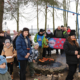 Galeria zdjęć z zimowych zajęć survivalowych, przedstawiająca dzieci i dorosłych podczas ogniska, wspólnego poczęstunku, pracy z mapą oraz ćwiczeń w terenie pokrytym śniegiem.