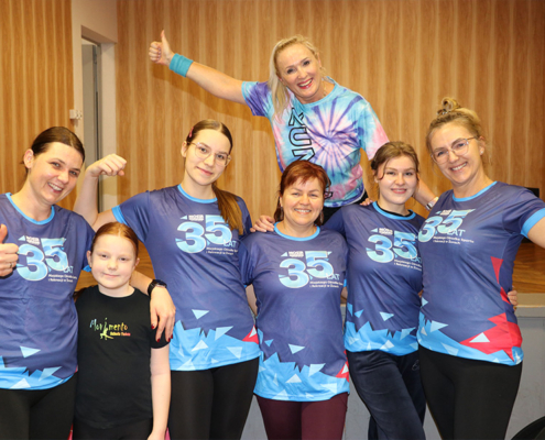 Galeria zdjęć z zajęć taneczno-fitness (Zumba) – wspólna rozgrzewka i choreografie prowadzone przez instruktorkę, aktywność uczestników w sali oraz integracyjne ujęcia zespołu MOSiR.