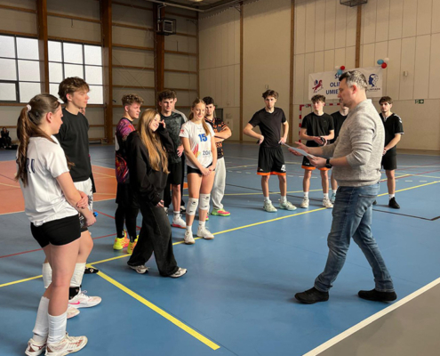 Galeria zdjęć z turnieju siatkówki młodzieży – odprawa drużyn przed meczami, dynamiczne akcje przy siatce, zagrywki i bloki oraz rywalizacja zespołów w hali sportowej.