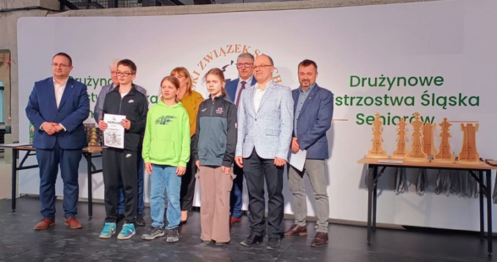 Galeria zdjęć z turnieju szachowego, przedstawiająca wręczenie nagród oraz uczestników rozgrywających partie przy stołach.