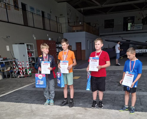 Galeria zdjęć przedstawiająca modele samolotów na trawiastym terenie. Widoczne są ujęcia z lotu ptaka, uczestnicy wydarzenia, przygotowane modele oraz moment wręczania nagród.